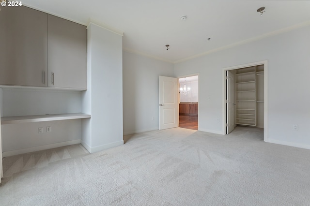 unfurnished bedroom featuring a chandelier, a walk in closet, light colored carpet, and crown molding