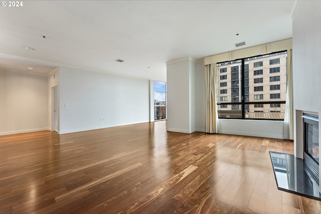 unfurnished living room featuring a wealth of natural light, wood-type flooring, and ornamental molding