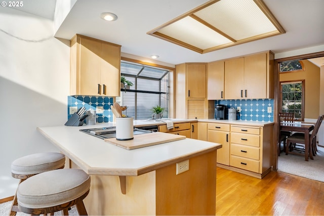 kitchen with kitchen peninsula, light brown cabinets, light hardwood / wood-style floors, and decorative backsplash