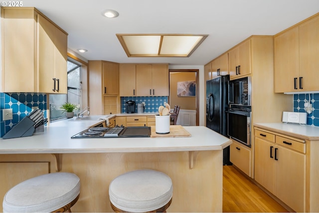 kitchen featuring a breakfast bar, backsplash, kitchen peninsula, light brown cabinetry, and black appliances