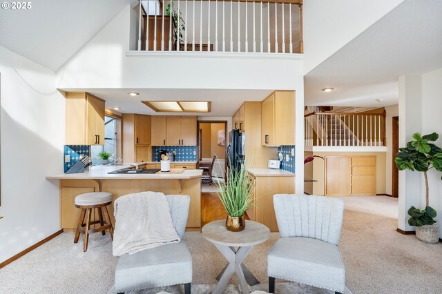 interior space with backsplash, a towering ceiling, light brown cabinetry, a kitchen bar, and kitchen peninsula