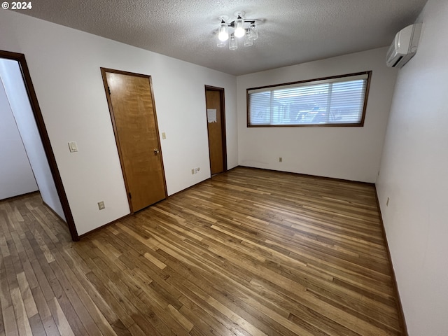 unfurnished bedroom featuring a wall mounted air conditioner, wood-type flooring, and a textured ceiling