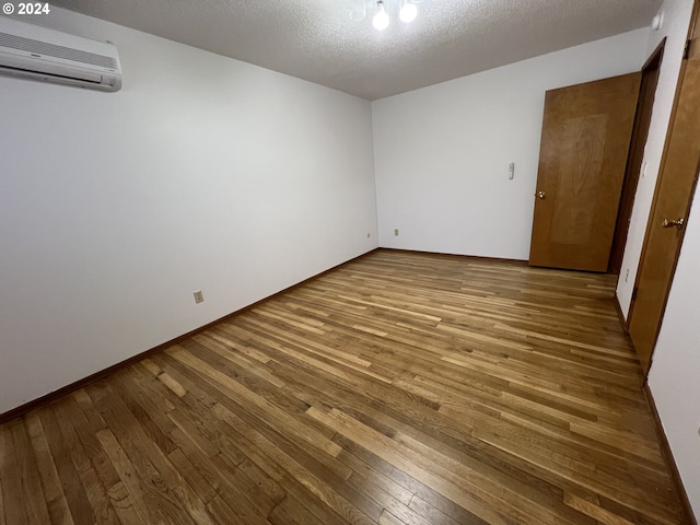 unfurnished room featuring wood-type flooring, a textured ceiling, and an AC wall unit