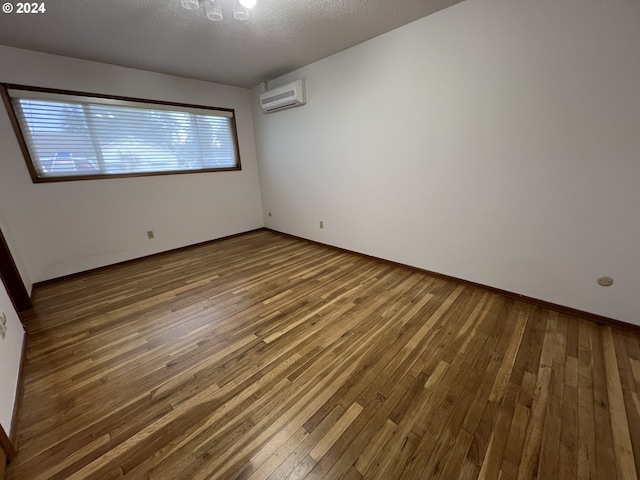 unfurnished room with wood-type flooring, a textured ceiling, and a wall unit AC