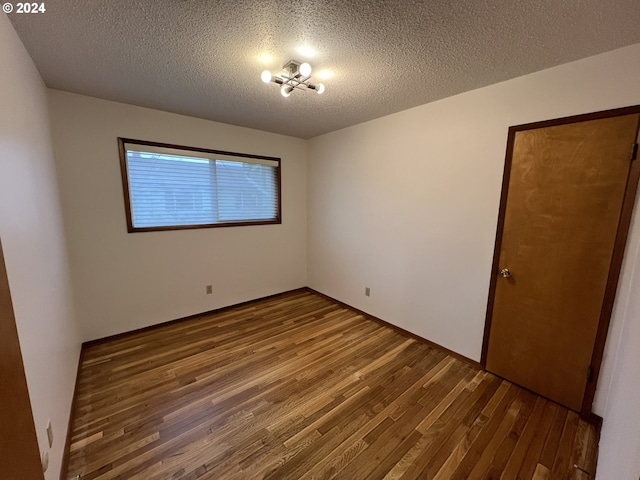 spare room with a chandelier, wood-type flooring, and a textured ceiling