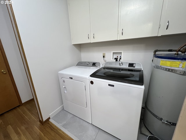 clothes washing area with hardwood / wood-style floors, cabinets, separate washer and dryer, and water heater