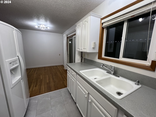 kitchen with a textured ceiling, sink, white cabinetry, white fridge with ice dispenser, and light tile patterned flooring