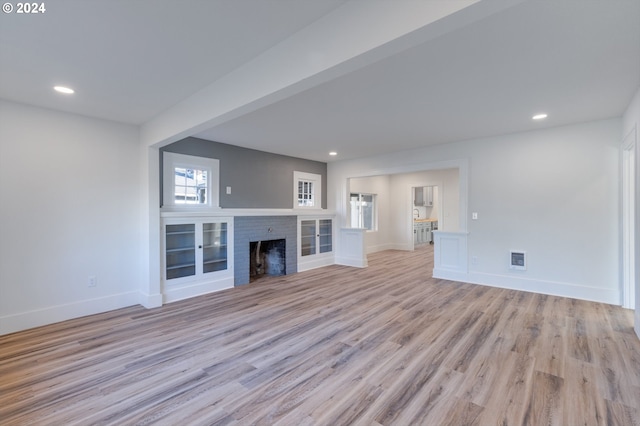 unfurnished living room with light wood-type flooring and a brick fireplace