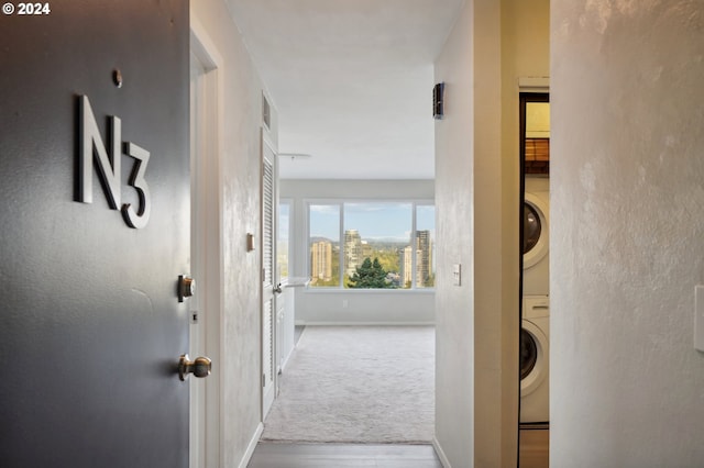 hall featuring baseboards, a view of city, carpet flooring, and stacked washing maching and dryer