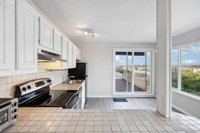 kitchen with under cabinet range hood, stainless steel electric stove, a healthy amount of sunlight, and tasteful backsplash