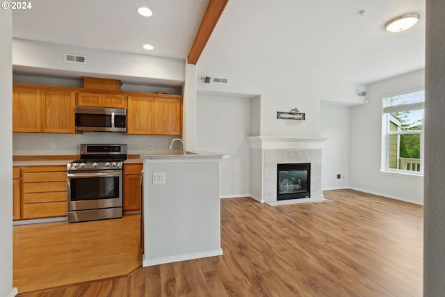 kitchen featuring sink, light wood-type flooring, a fireplace, appliances with stainless steel finishes, and beam ceiling