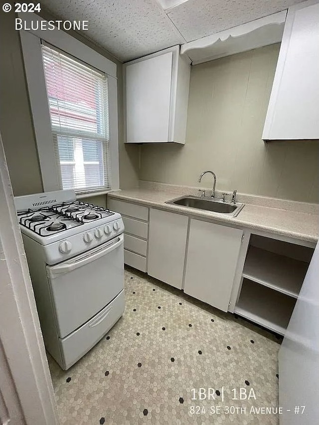 kitchen featuring white cabinets, white gas range, and sink