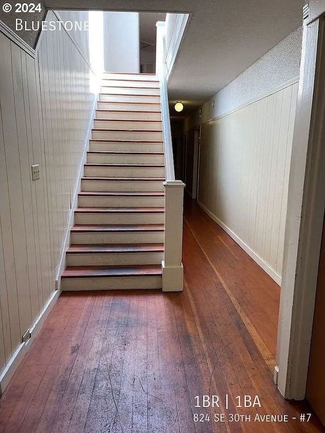 stairs with a textured ceiling, wooden walls, and hardwood / wood-style floors