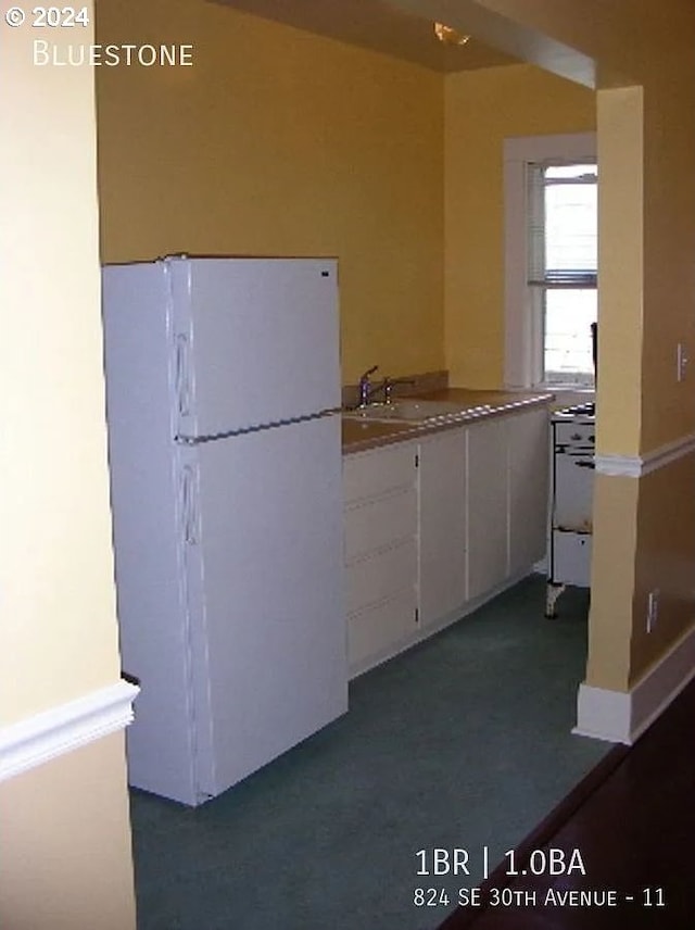 kitchen featuring dark carpet, white cabinets, and white fridge