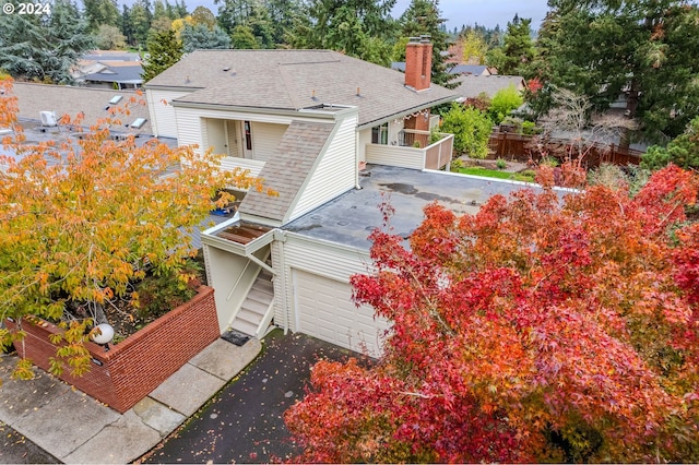 rear view of property featuring aphalt driveway, a garage, fence, roof with shingles, and a chimney