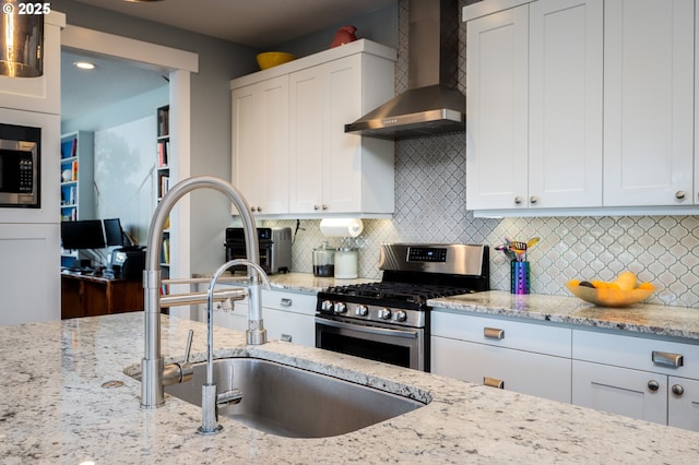 kitchen with wall chimney exhaust hood, tasteful backsplash, stainless steel appliances, light stone countertops, and white cabinets