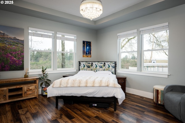 bedroom featuring an inviting chandelier, dark hardwood / wood-style floors, and a raised ceiling