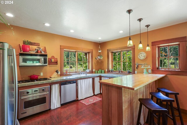 kitchen featuring pendant lighting, dark wood-type flooring, sink, a kitchen bar, and appliances with stainless steel finishes