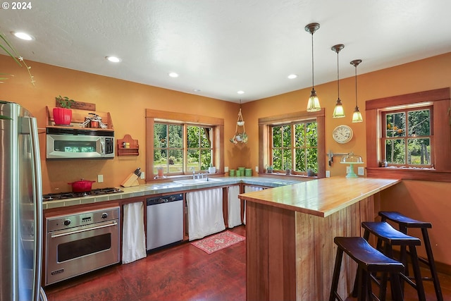 kitchen featuring tile countertops, recessed lighting, stainless steel appliances, a sink, and a kitchen bar