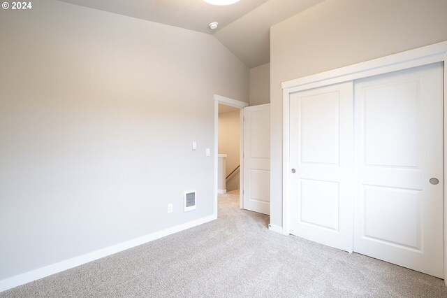 unfurnished bedroom with light carpet, vaulted ceiling, and a closet