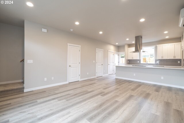 unfurnished living room with a wall mounted air conditioner and light hardwood / wood-style flooring