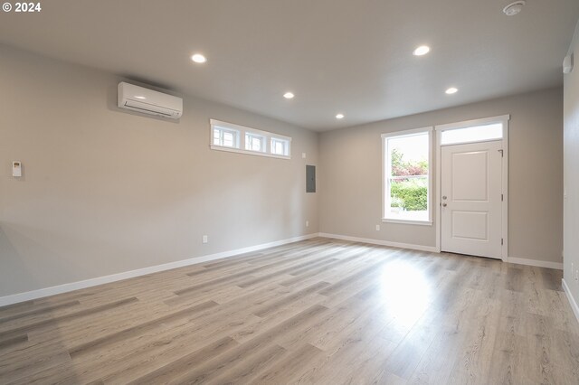 empty room featuring light wood-type flooring, electric panel, and a wall unit AC