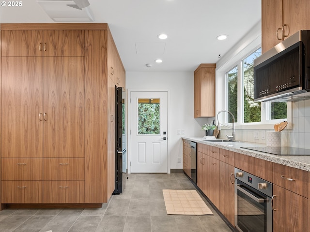 kitchen featuring light stone counters, sink, decorative backsplash, and black appliances