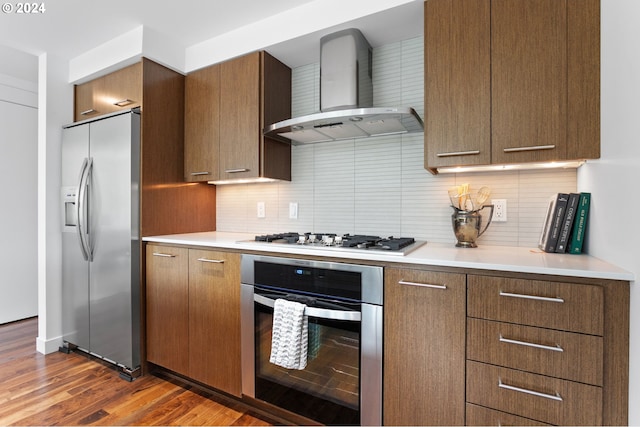 kitchen featuring appliances with stainless steel finishes, wall chimney range hood, tasteful backsplash, and dark hardwood / wood-style flooring