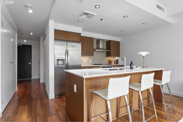 kitchen featuring an island with sink, dark wood-type flooring, sink, wall chimney exhaust hood, and stainless steel appliances