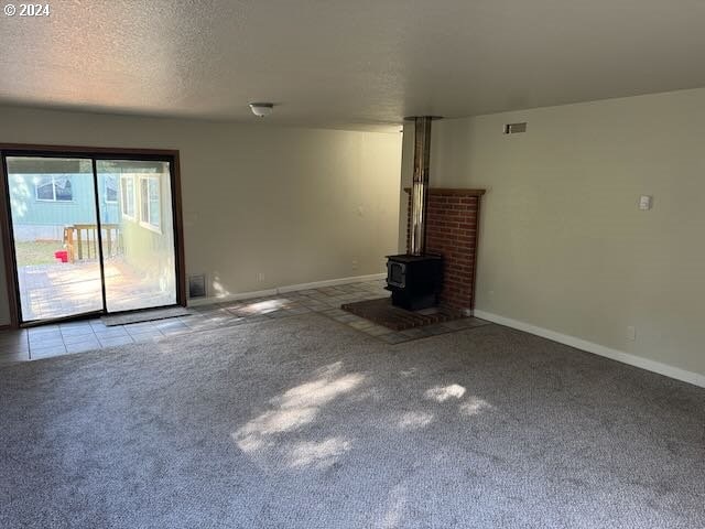 unfurnished living room with a wood stove, light colored carpet, and a textured ceiling