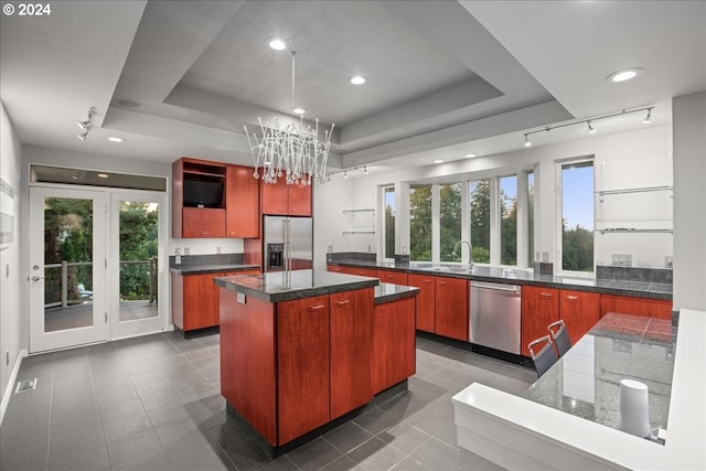 kitchen featuring appliances with stainless steel finishes, a center island, a tray ceiling, sink, and an inviting chandelier