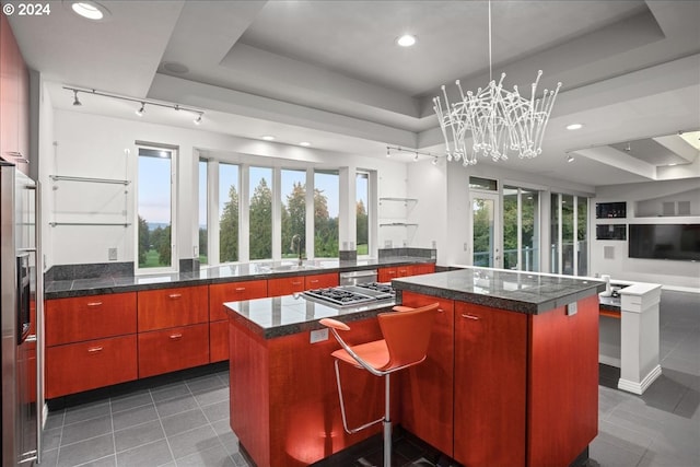 kitchen featuring track lighting, a raised ceiling, a center island, dark tile patterned floors, and sink