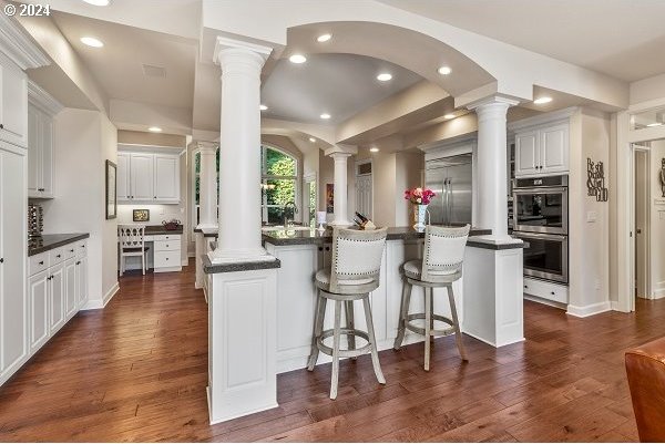 kitchen with dark wood-type flooring, kitchen peninsula, stainless steel appliances, and white cabinets