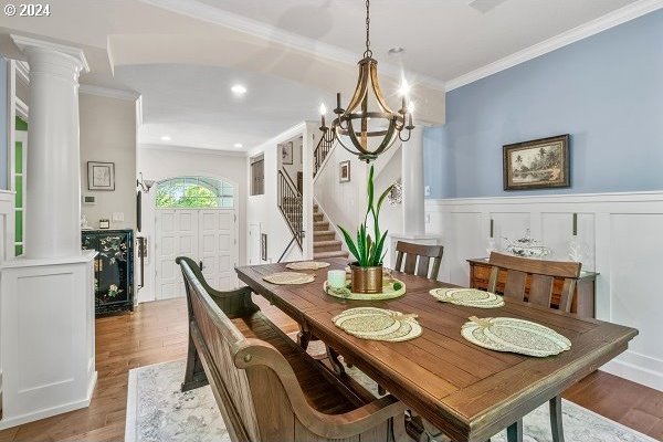 dining room with an inviting chandelier, decorative columns, hardwood / wood-style floors, and crown molding