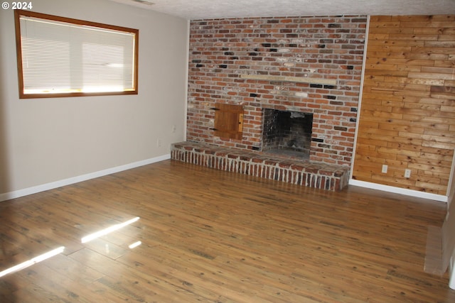 unfurnished living room featuring hardwood / wood-style floors, a brick fireplace, and a textured ceiling