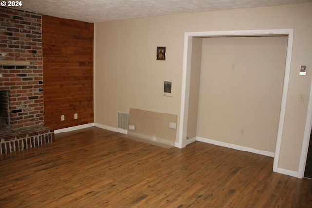 unfurnished living room with a textured ceiling, wooden walls, a fireplace, and dark hardwood / wood-style floors