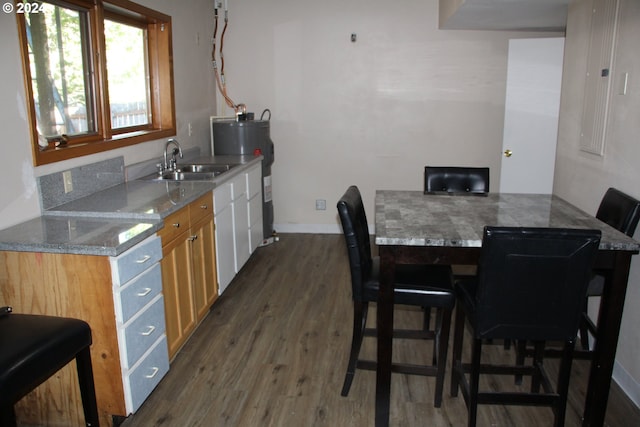 kitchen featuring light stone countertops, sink, dark hardwood / wood-style flooring, water heater, and a breakfast bar area