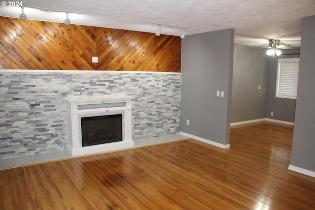 unfurnished living room with hardwood / wood-style floors, track lighting, ceiling fan, a textured ceiling, and wood walls