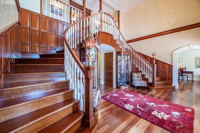 stairs with ornate columns, a towering ceiling, and hardwood / wood-style flooring