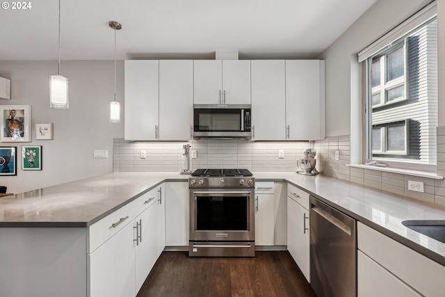 kitchen featuring kitchen peninsula, appliances with stainless steel finishes, dark wood-type flooring, pendant lighting, and white cabinets