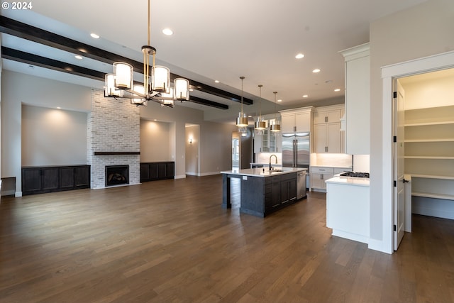 kitchen featuring white cabinets, a fireplace, an island with sink, decorative light fixtures, and dark hardwood / wood-style flooring