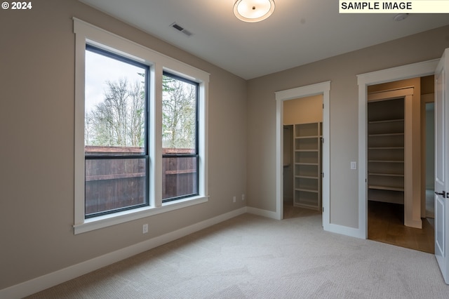 unfurnished bedroom with a spacious closet, a closet, and light carpet