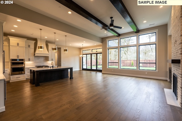 kitchen featuring dark wood-type flooring, a center island with sink, a fireplace, custom range hood, and stainless steel appliances