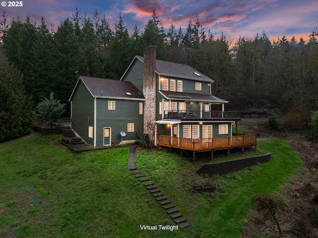 back house at dusk featuring a deck and a lawn