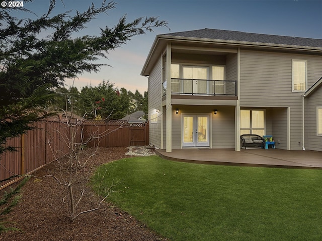 back house at dusk featuring french doors, a yard, a balcony, and a patio area