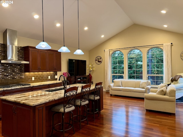 kitchen with backsplash, wall chimney range hood, an island with sink, dark hardwood / wood-style flooring, and stainless steel gas cooktop