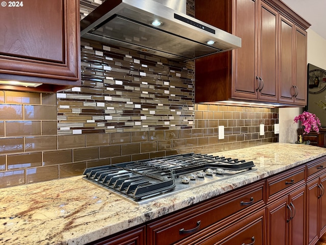 kitchen with tasteful backsplash, light stone counters, stainless steel gas stovetop, and wall chimney range hood