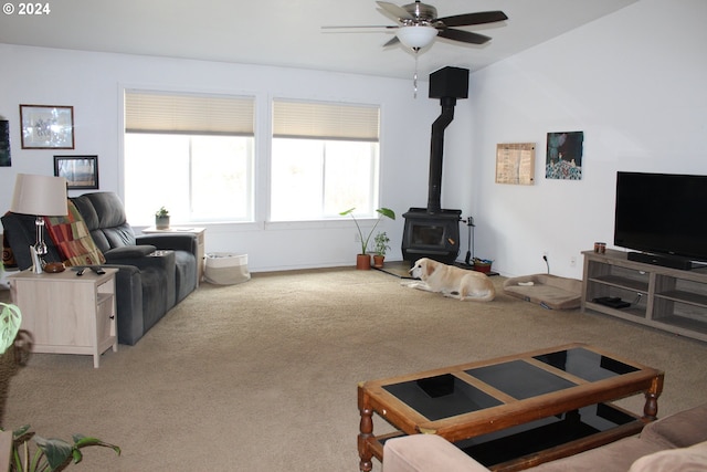 carpeted living room with ceiling fan, a wood stove, and vaulted ceiling