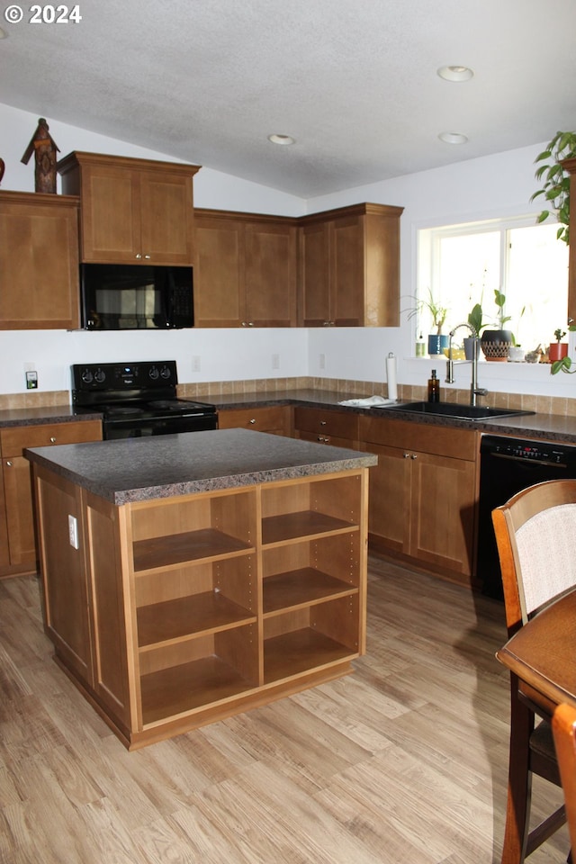 kitchen featuring vaulted ceiling, black appliances, sink, light hardwood / wood-style floors, and a center island