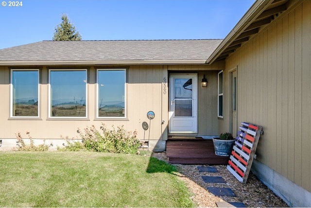 entrance to property featuring a lawn and roof with shingles